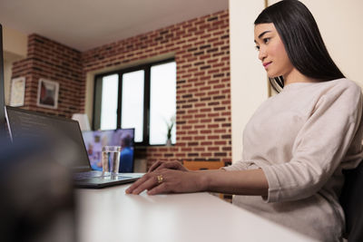 Side view of woman using laptop at home