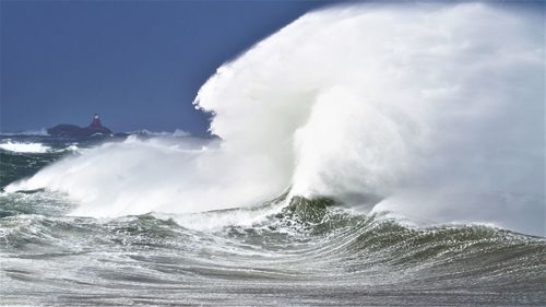 Waves splashing on shore against sky