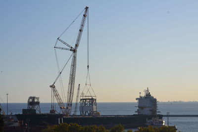 Cranes at commercial dock against clear sky