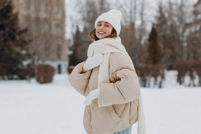 Portrait of smiling young woman standing on snow covered field