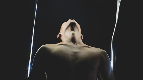 Low angle view of shirtless man standing against black background