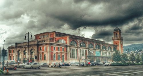 Road passing through city against cloudy sky