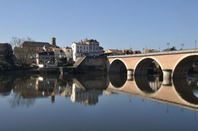 Arch bridge over river by buildings against clear sky