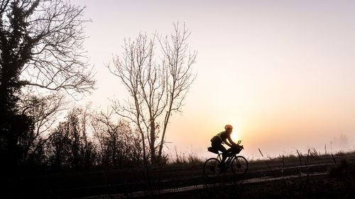 Man riding bicycle against sky during sunset