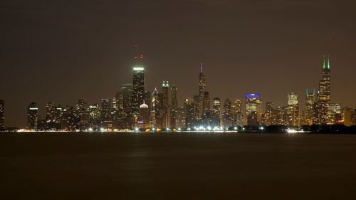 Sea by illuminated city skyline against sky at night