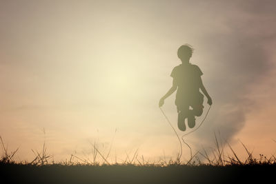 Silhouette girl skipping on field against sky during sunset