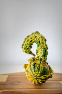 A image of a unusually shaped green and yellow pumpkin standing on a wooden chopping board