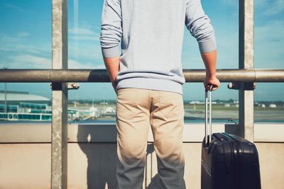 Midsection of man holding luggage while waiting at airport