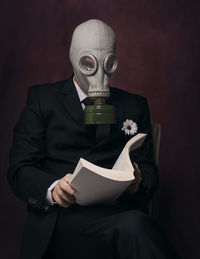 Man wearing gas mask while reading book against black background