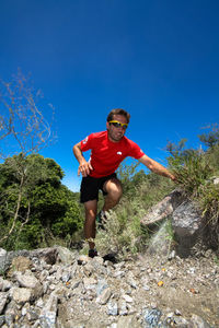 Full length of young man standing on rocks against blue sky