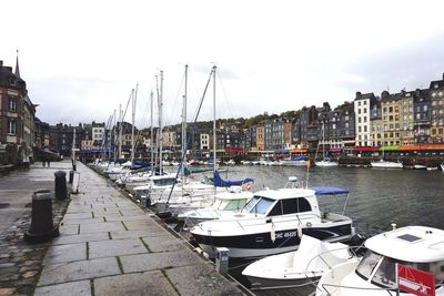 Sailboats moored on harbor in city against sky