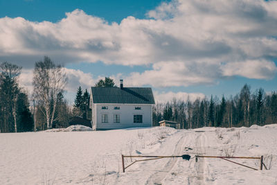 Snow covered field by building against sky