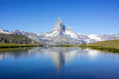 Scenic view of lake and mountains against clear blue sky