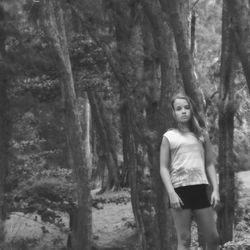 Portrait of woman standing by tree trunk in forest