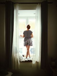 Full length rear view of woman standing at home