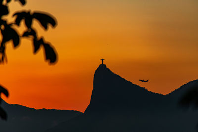 Silhouette birds flying against orange sky