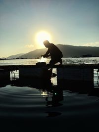 Silhouette man standing on shore against sky during sunset