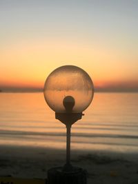 Street light by sea against sky during sunset