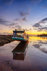 Boat moored in lake against sky during sunset