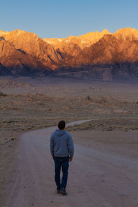 Rear view of man standing on road leading to mountains