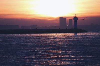 Silhouette buildings by sea against sky during sunset