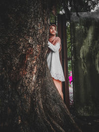 Portrait of woman standing by tree trunk