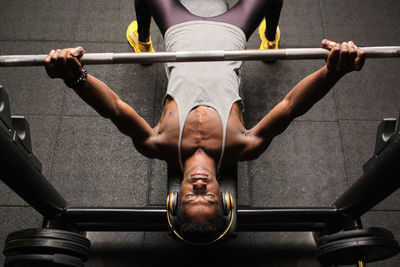 Determined young man doing bench press while listening music through headphones in gym