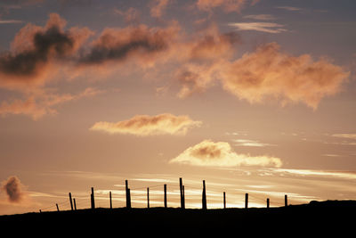 Silhouette of fence posts at sunrise with cloudy sky