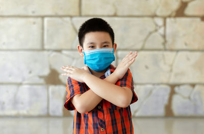 Portrait of boy wearing flu mask gesturing while standing against wall