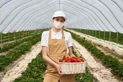 Young woman holding apple while standing in basket
