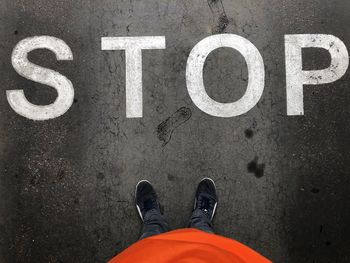 Low section of man standing by stop sign on road