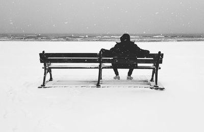 Rear view of man sitting on bench in winter