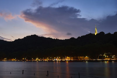 Illuminated buildings by river against sky at night