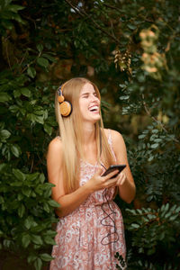 Beautiful young woman using phone while standing on plant