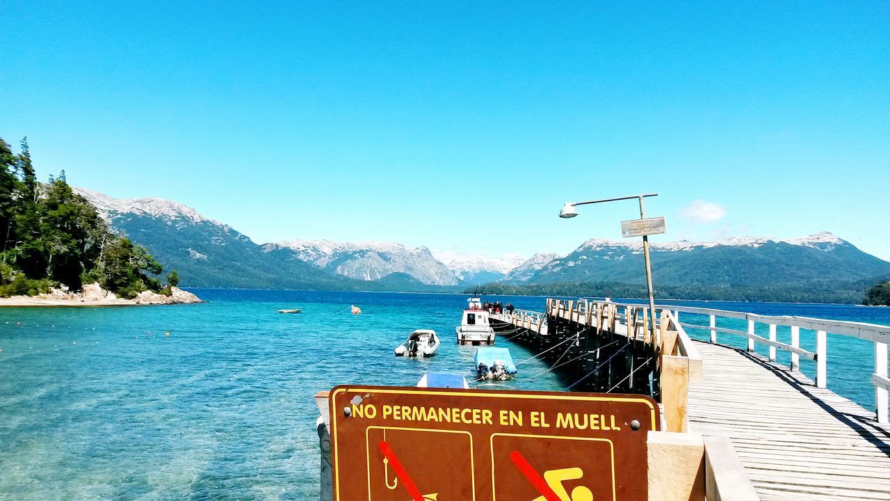 water, clear sky, mountain, sea, blue, copy space, text, scenics, tranquility, tranquil scene, nature, beauty in nature, communication, transportation, mountain range, day, western script, railing, sign, guidance