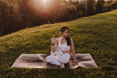 Woman practicing yoga on field during sunset