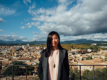 Portrait of smiling young woman standing against buildings in city