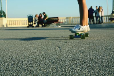 Low section of woman skateboarding on road against clear blue sky during sunset