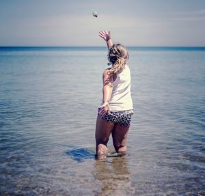 Rear view of girl playing in sea against sky