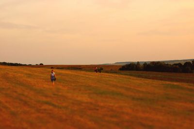 Rear view of girl walking on landscape against sky during sunset