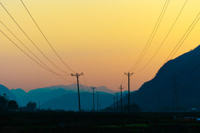 Silhouette electricity pylons against sky during sunset