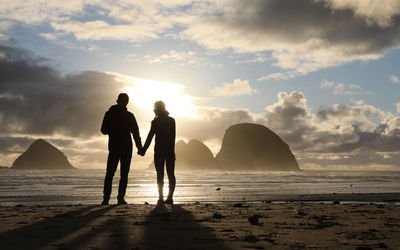 Couple standing on beach against sky during sunset