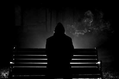 Rear view of silhouette woman sitting on bench at night