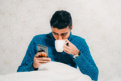 Young man using mobile phone while sitting on bed