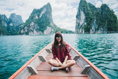 Young woman sitting by lake against mountain