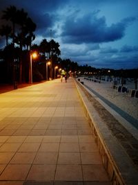 Illuminated footpath by street against sky at night