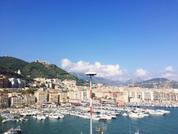 Boats moored in sea by cityscape against blue sky