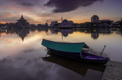 Boats in river against buildings during sunset