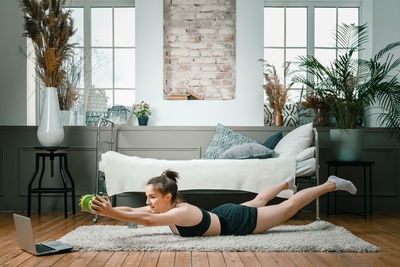 Positive athletic woman with neatly tied hair and tight sportswear holds the plank with dumbbells 