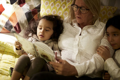 High angle view of grandmother reading book to granddaughters while lying on bed at home